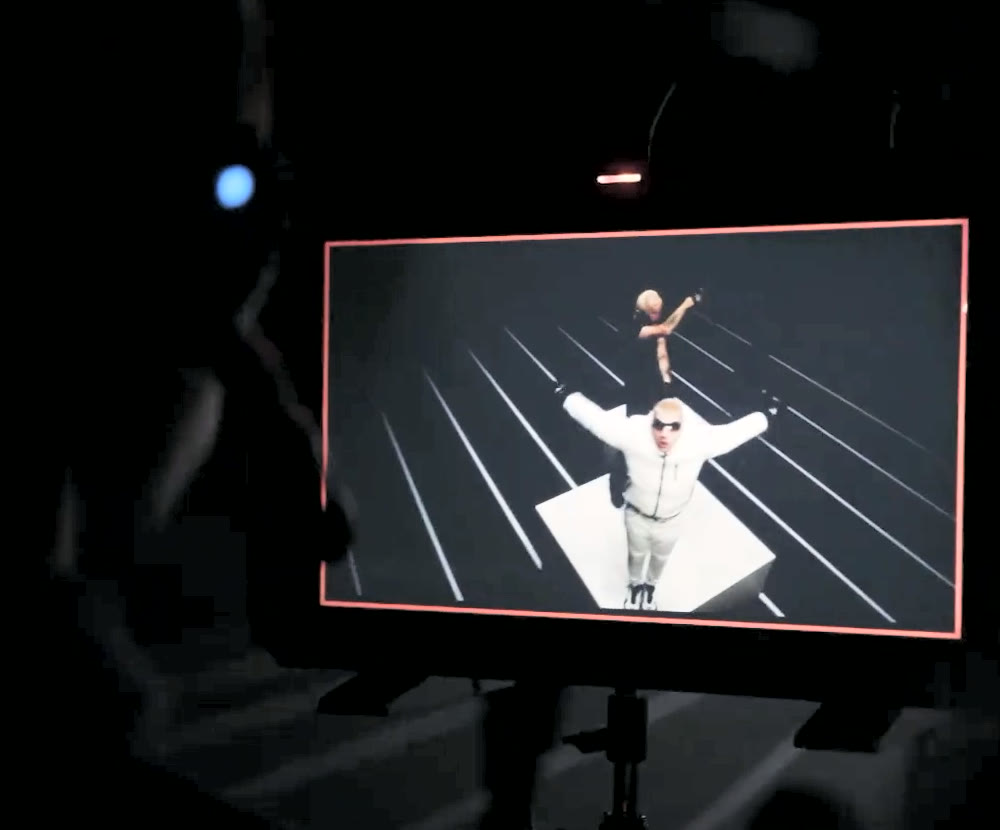 A dark set: an operator in a glowing headset beside a playback monitor showing a performer in white